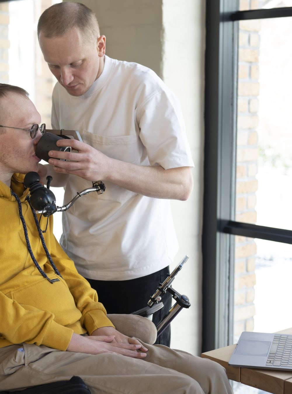 Aide à domicile aidant un homme en situation de Handicap à boire à son domicile