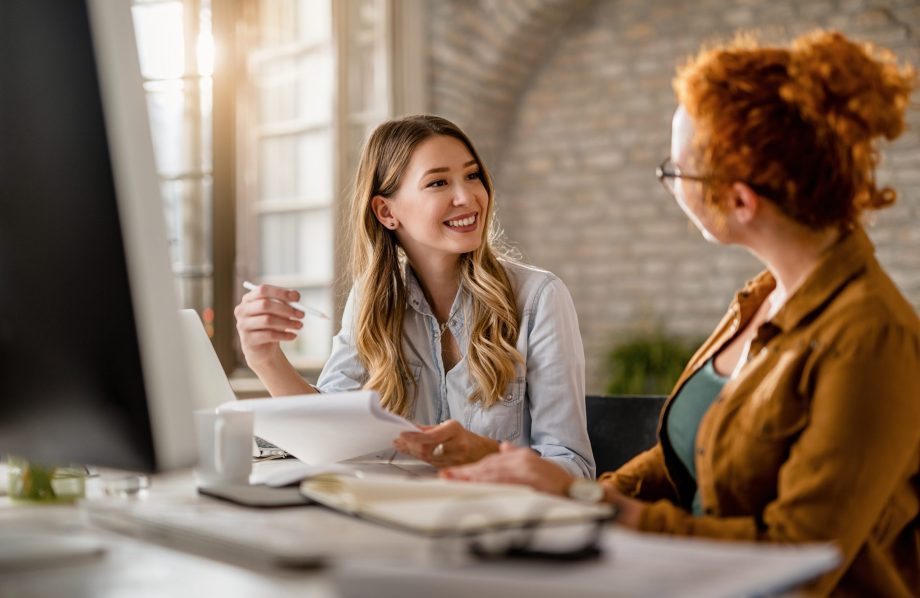 Entretien entre une femme blonde souriante qui prend des notes et une femme rousse de dos