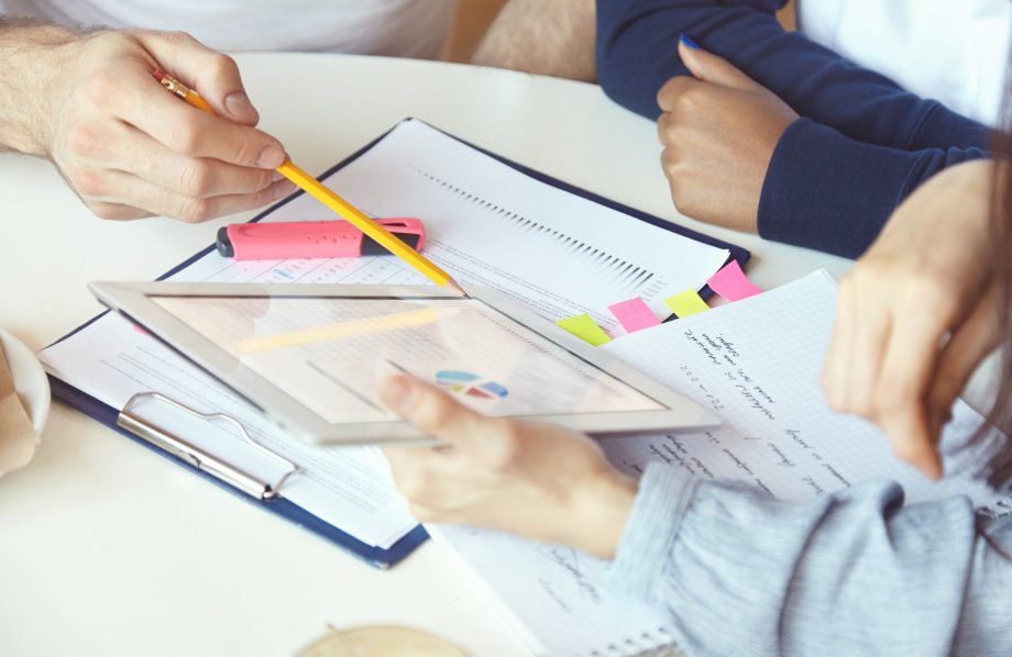 Mains de deux personnes travaillant à un bureau et analysant des documents comportant des graphiques.