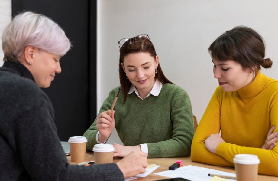 Trois femmes en réunion autour d'une table avec des cafés et des documents imprimés